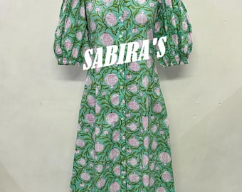Puede incluir: Un vestido verde con botones y un estampado floral en rosa y blanco. El vestido tiene mangas cortas abullonadas y cuello camisero. El texto "SABIRA'S" está impreso en la parte delantera del vestido.