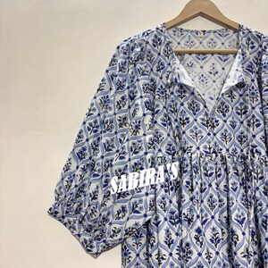 May include: A light blue and white patterned dress with short sleeves. The dress features a floral design and the text "SABIRA'S" in white. The dress is hanging on a wooden hanger.