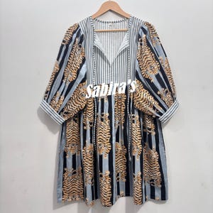May include: A knee-length dress featuring a tiger print pattern over vertical black and light blue stripes. The garment has three-quarter length sleeves with striped cuffs, a V-neckline with a tie closure, and the text sabira's printed in white.