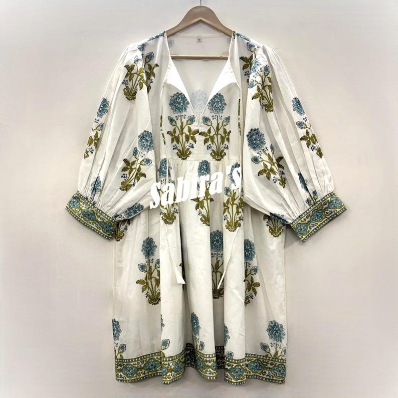 Pu&ograve; includere: Abito bianco con stampa floreale blu e verde. L'abito presenta uno scollo a V, maniche lunghe con polsini elasticizzati e una gonna a balze. Il motivo floreale &egrave; ripetuto su tutto l'abito, con un bordo sulle maniche e sull'orlo.