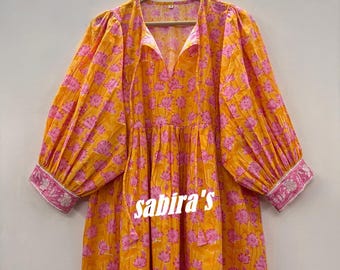 May include: A long-sleeved, V-neck dress in a vibrant orange hue, adorned with a repeating pink floral pattern. The dress features voluminous sleeves and a pink and silver embroidered cuff. The text "sabira's" is visible on the dress.