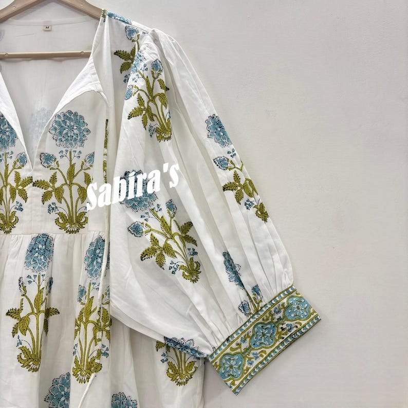 Pu&ograve; includere: Top tunica bianco con stampa floreale blu e verde. Il top presenta uno scollo a V, maniche lunghe e la scritta "Sabira's" sul davanti. Le maniche e l'orlo sono rifiniti con un bordo fantasia.