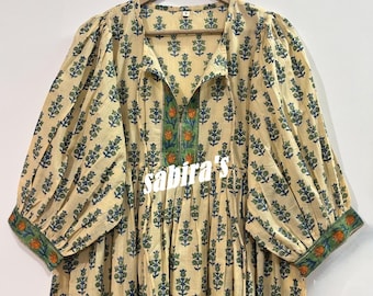 Puede incluir: Vestido color crema de manga larga con un estampado floral azul y verde. El vestido presenta un escote en V con un borde floral verde y naranja, y las mangas tienen ribetes verdes y naranjas. El texto "sabira's" es visible.