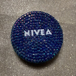 Może przedstawiać: Okrągły, niebieski, błyszczący pojemnik z napisem "NIVEA" białymi literami.