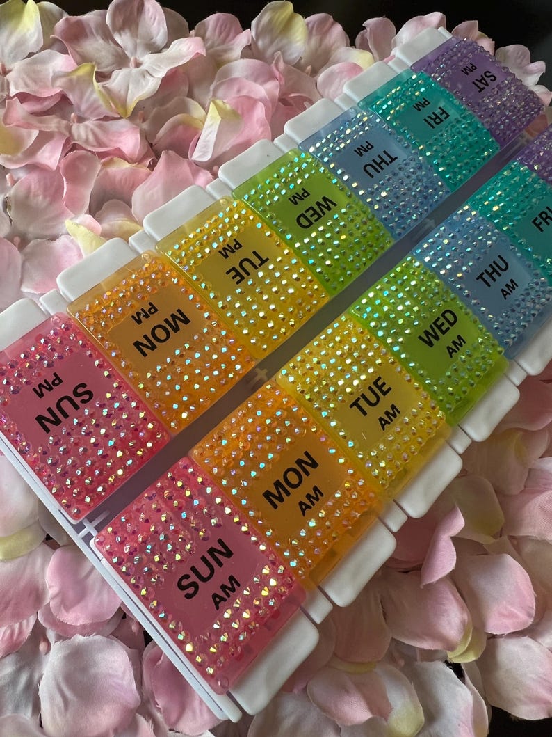 Puede incluir: Un organizador de pastillas para siete d&iacute;as con una caja de pl&aacute;stico transparente y compartimentos coloridos. Cada compartimento est&aacute; decorado con diamantes de imitaci&oacute;n y etiquetado con los d&iacute;as de la semana y AM o PM.