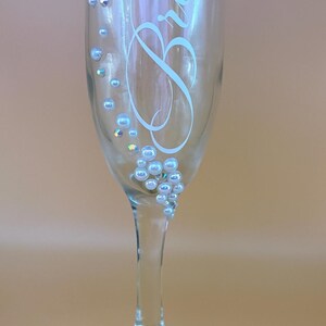 Puede incluir: Una copa de champ&aacute;n transparente con la palabra "Bride" en una elegante escritura. El cristal est&aacute; adornado con pedrer&iacute;a iridiscente y adornos perlados, a&ntilde;adiendo un toque de brillo. Perfecto para una boda o celebraci&oacute;n nupcial.