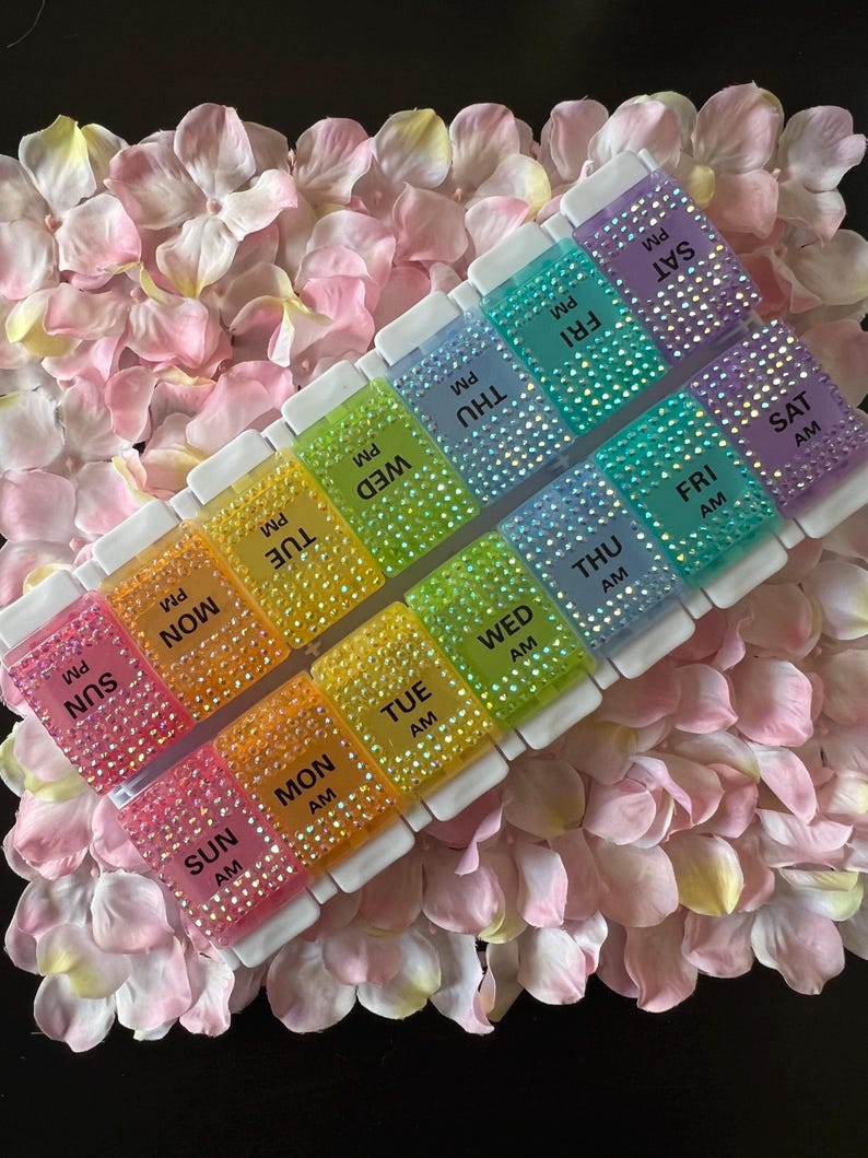 Puede incluir: Un organizador de pastillas para siete d&iacute;as con compartimentos para cada d&iacute;a de la semana, etiquetados con los d&iacute;as de la semana y AM o PM. Los compartimentos est&aacute;n decorados con brillantes de colores.