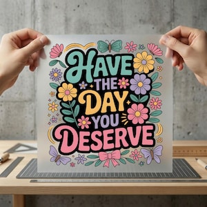 May include: A colorful graphic with the text "Have the day you deserve" surrounded by flowers, butterflies, and a bow. The design features a retro aesthetic with a black background and pastel colors.
