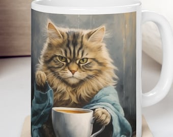 May include: White ceramic mug with a brown and white cat holding a white mug with brown liquid. The cat is wearing a blue robe and has a serious expression. The mug is on a beige coaster.