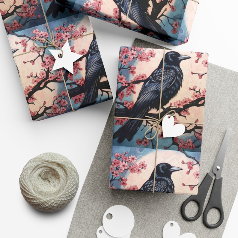 May include: Three gift wrap designs featuring black birds perched on branches with pink blossoms. The designs are on a light blue background with white accents.