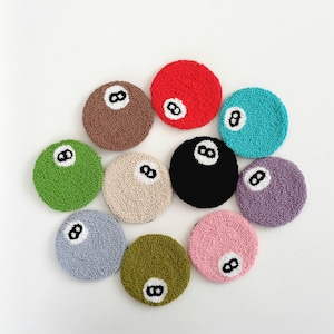 Può includere: Una collezione di dieci sottobicchieri circolari trapuntati in vari colori, tra cui rosso, nero, marrone, verde, blu, viola, grigio, beige, oliva e rosa. Ogni sottobicchiere presenta una toppa circolare bianca con un numero otto nero ricamato.