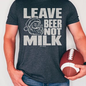 A person wearing a dark grey t-shirt that reads LEAVE BEER NOT MILK with a Santa graphic, holding a football.