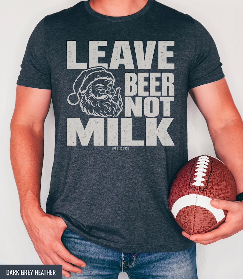 A person wearing a dark grey t-shirt that reads LEAVE BEER NOT MILK with a Santa graphic, holding a football.