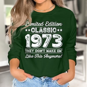 May include: A dark green sweatshirt with white text that reads "Limited Edition CLASSIC 1973 THEY DON'T MAKE EM' Like This Anymore!". The long-sleeved shirt has a crew neck and is made of a soft material.