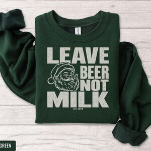 Dark green crewneck sweatshirt featuring a graphic of Santa holding a beer with text that reads Leave Beer Not Milk.