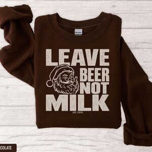 Dark brown crewneck sweatshirt featuring a graphic of winking Santa drinking beer with text Leave Beer Not Milk.