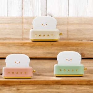 May include: Three miniature toasters with smiling bread faces. The toasters are white, pink, and green with gold trim. Each toaster has the word "TOAST" printed on the front.