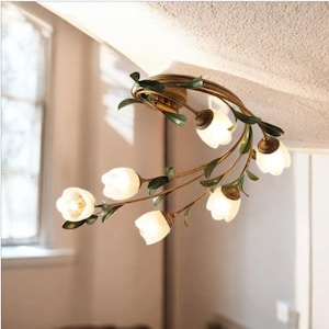 May include: A gold ceiling light fixture with a floral design. The light fixture has six white glass bulbs shaped like tulips and green leaves.