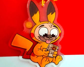 Peut inclure: Un porte-clés en acrylique transparent représentant un personnage de dessin animé déguisé en Pikachu, tenant une console de jeu portable. Le porte-clés a un fermoir jaune et un code couleur jaune et orange, sur fond rouge.