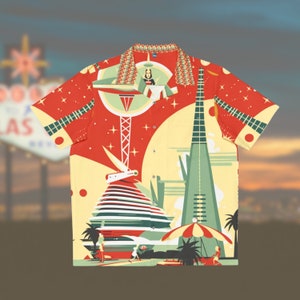Op de afbeelding: Een rood, geel en groen kort mouw overhemd met knopen en een retro-ontwerp met een ruimteschip, een hoog gebouw en palmbomen. Het shirt heeft een sterrenpatroon en de tekst "LAS" is zichtbaar op de achtergrond.