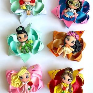 May include: Five handmade hair bows featuring different Disney princesses. Each bow is made with colorful ribbon and features a unique princess character with a detailed face and outfit. The princesses include Ariel, Tiana, Belle, Jasmine, and Snow White.