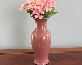 May include: A mauve ceramic vase with a wide mouth and a narrow base, holding a bouquet of pink artificial flowers.