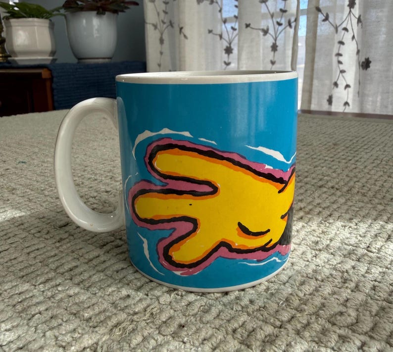 Peut inclure: Mug en c&eacute;ramique avec une anse blanche et un ext&eacute;rieur bleu vif. Le mug pr&eacute;sente un motif de main jaune avec des contours roses et noirs. Convient aux boissons chaudes ou froides. Capacit&eacute; d'environ 300 ml.