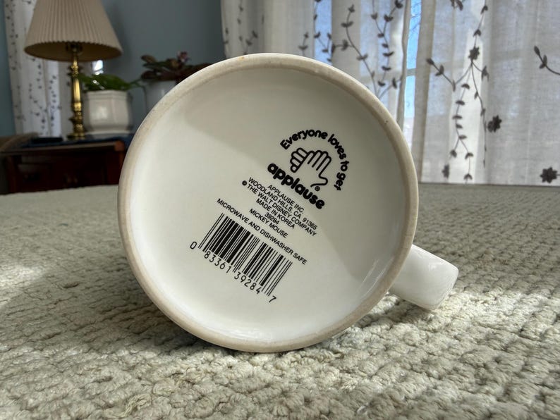 Peut inclure: Mug en c&eacute;ramique blanche avec une anse, portant l'inscription "Everyone loves to get applause" et un code-barres. Le mug est marqu&eacute; comme allant au micro-ondes et au lave-vaisselle. Le fond du mug est visible.