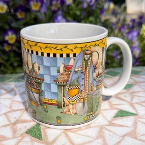 May include: A white ceramic mug with a wraparound illustration featuring a garden scene with a blue checkered background, a coat, and a straw hat. The mug has a yellow border with a floral design and a white handle.