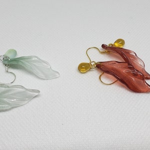 May include: A pair of green leaf-shaped earrings with a light green stone and a pair of red leaf-shaped earrings with a yellow stone.