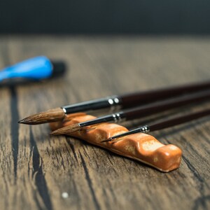 Brown paint brush holder, brushes and paint on wooden table.