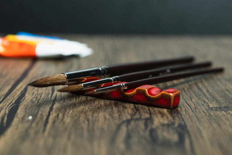 Red paint brush holder with brushes on a wooden table.