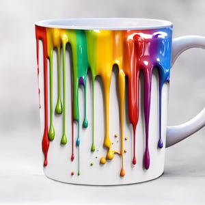 Może przedstawiać: Biały ceramiczny kubek z tęczową farbą spływającą po boku. Farba jest w kolejności: czerwony, pomarańczowy, żółty, zielony, niebieski i fioletowy.