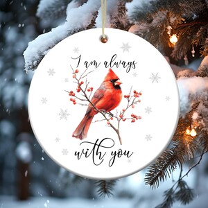 May include: White ceramic ornament with a red cardinal perched on a branch with red berries. The ornament has the text "I am always with you" in black cursive lettering.