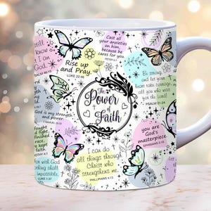 May include: White ceramic mug with a colorful design featuring butterflies, flowers, and inspirational quotes about faith. The mug has a black outline and the text "The Power of Faith" in a black circle.