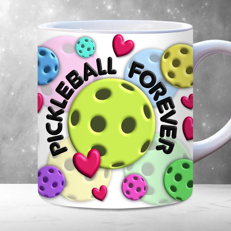 Puede incluir: Taza de caf&eacute; de cer&aacute;mica blanca con un dise&ntilde;o colorido que presenta palas de pickleball, corazones y el texto "Pickleball Forever".