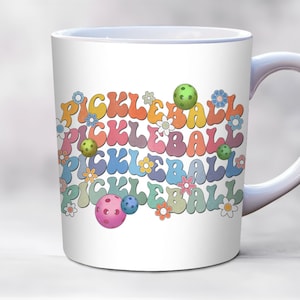 May include: White ceramic mug with a colorful design of the word "pickleball" repeated multiple times in a rainbow pattern with green, pink, and blue pickleballs.