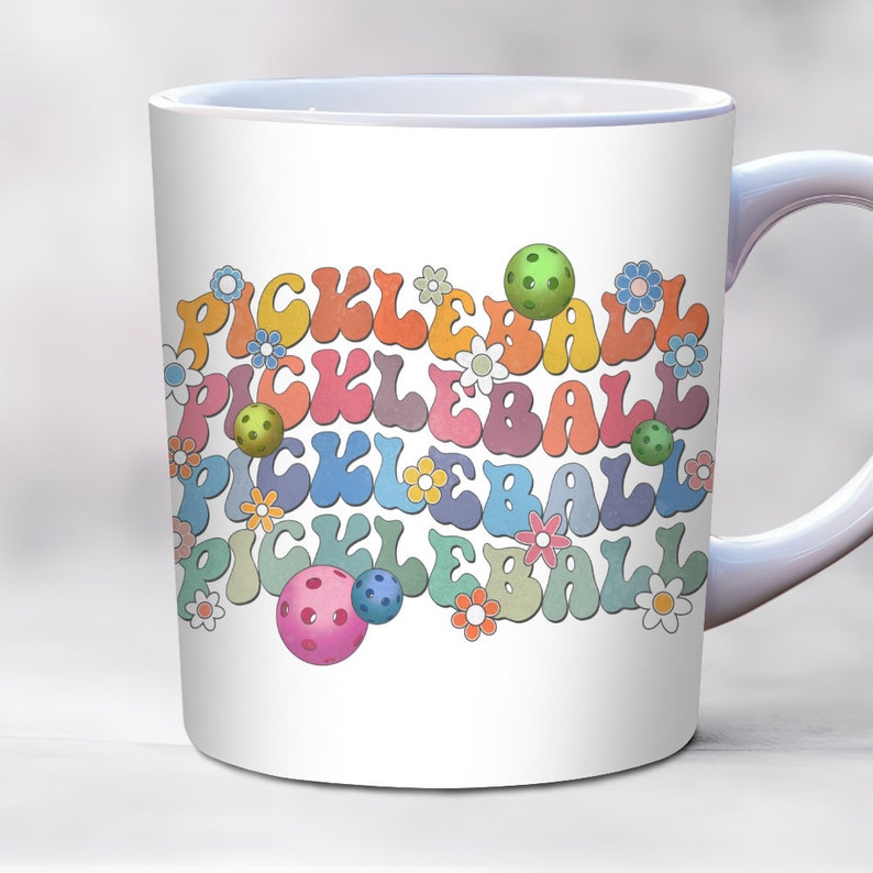 May include: White ceramic mug with a colorful design of the word "pickleball" repeated multiple times in a rainbow pattern with green, pink, and blue pickleballs.