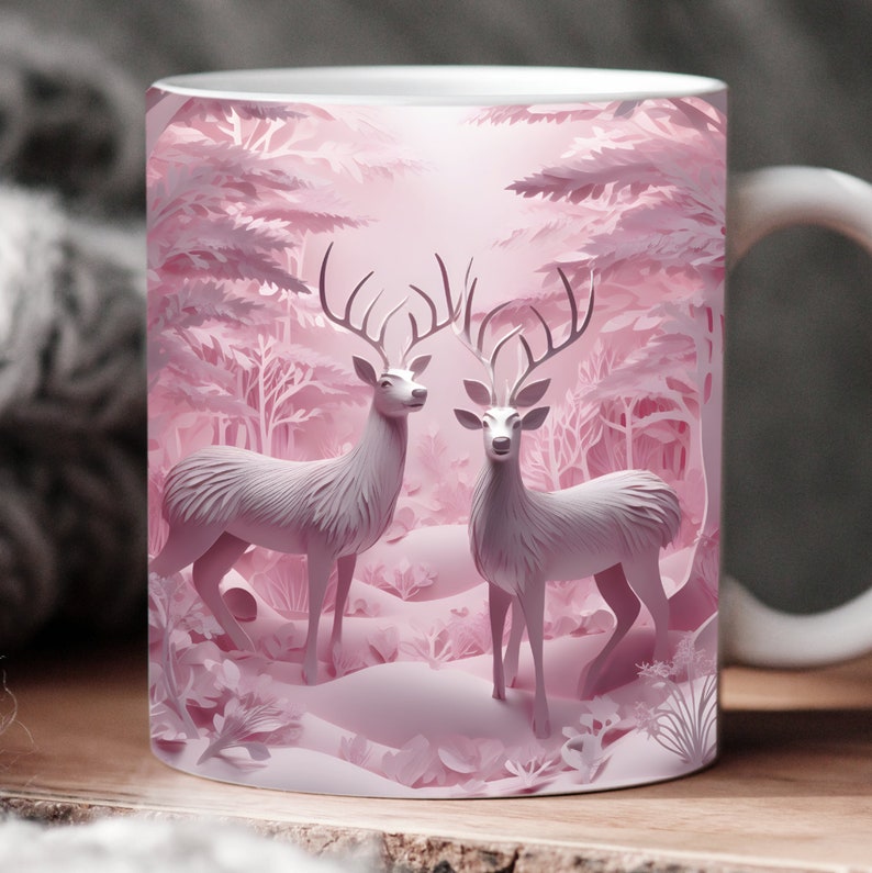 Puede incluir: Una taza de cer&aacute;mica blanca con un dise&ntilde;o de papel recortado rosa de dos ciervos de pie en un bosque nevado. Los ciervos tienen cuernos y se miran el uno al otro.