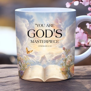 Puede incluir: Taza de cerámica blanca con un diseño de cielo y nubes. La taza presenta el texto "You are God's Masterpiece" con la referencia bíblica "Efesios 2:10".