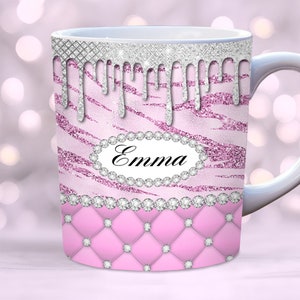 May include: Pink and silver glitter mug with a zebra print design and a diamond-shaped border. The mug has a white handle and the name "Emma" is written in black on a silver oval with rhinestones.