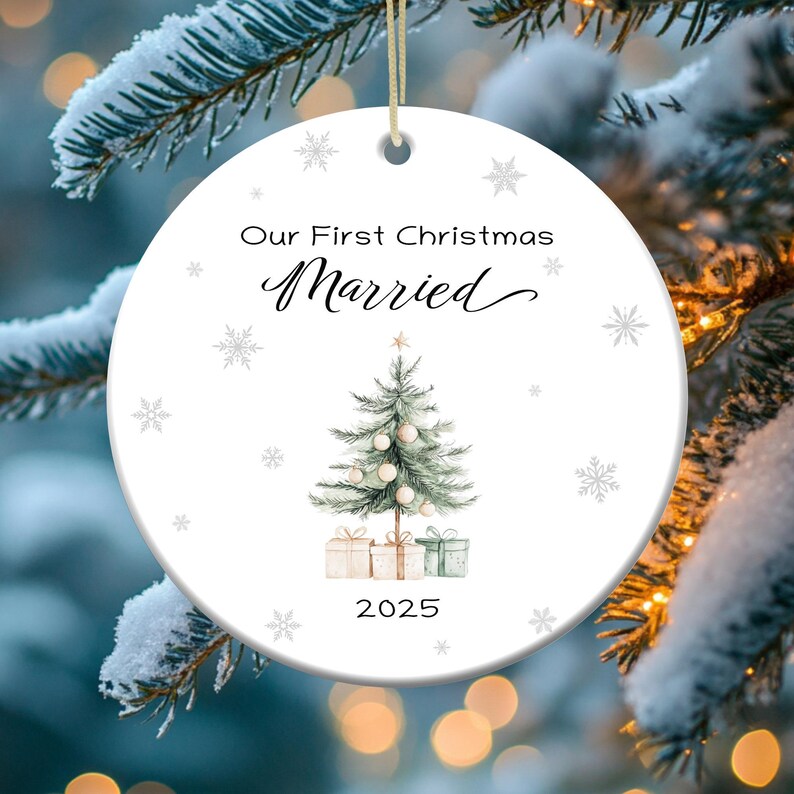 May include: White round Christmas ornament with a watercolor illustration of a Christmas tree with presents underneath. The ornament has the text "Our First Christmas Married 2025" on it.