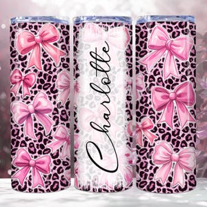 May include: A pink and black tumbler with a leopard print background and pink bows. The tumbler has the name "Charlotte" written on it.