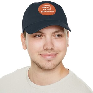 May include: A navy blue baseball cap with a brown leather patch. The patch features the text "I'm not SPECIAL I'm just DIFFERENT" in white lettering. The cap is worn by a person.