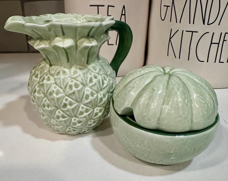 Może przedstawiać: Zielony ceramiczny dzbanek w kształcie ananasa i zielona ceramiczna cukiernica w kształcie limonki z pokrywką.