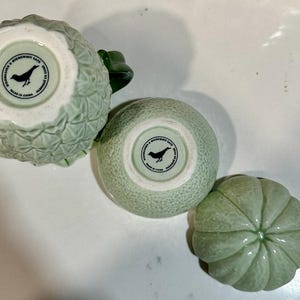 Może przedstawiać: Trzy zielone ceramiczne miski z wzorem ptaka i napisem "Made in China" na spodzie. Miski mają kształt ananasa, cytrus&oacute;w i melona.