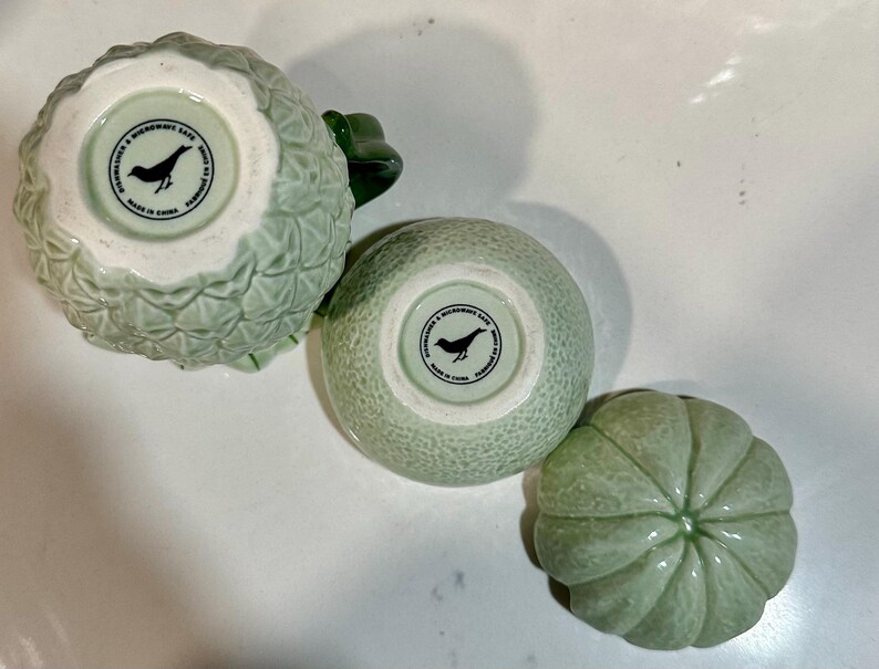 Może przedstawiać: Trzy zielone ceramiczne miski z wzorem ptaka i napisem "Made in China" na spodzie. Miski mają kształt ananasa, cytrus&oacute;w i melona.