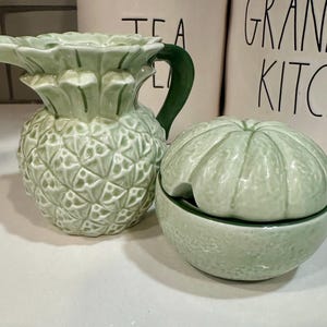 Może przedstawiać: Zielony ceramiczny dzbanek do śmietanki w kształcie ananasa i zielony ceramiczny cukiernica w kształcie limonki z pokrywką.