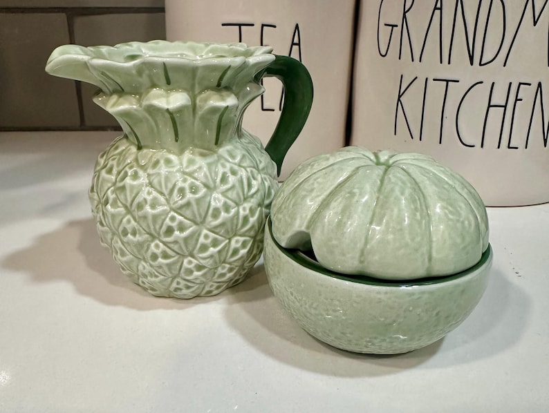 Może przedstawiać: Zielony ceramiczny dzbanek do śmietanki w kształcie ananasa i zielony ceramiczny cukiernica w kształcie limonki z pokrywką.