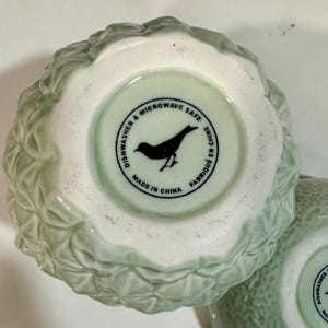 Może przedstawiać: Zielona ceramiczna miska z liściastym wzorem. Na spodzie miski znajduje się biała etykieta z czarnym tekstem: "Dishwasher & Microwave Safe Made in China Fabriqu&eacute; en Chine".